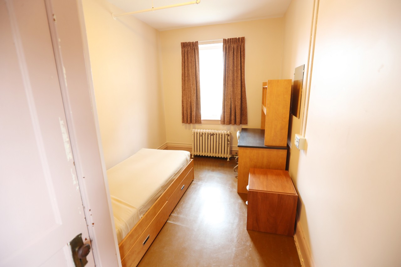 The single room has a bed, desk, storage drawers, and a closet. 