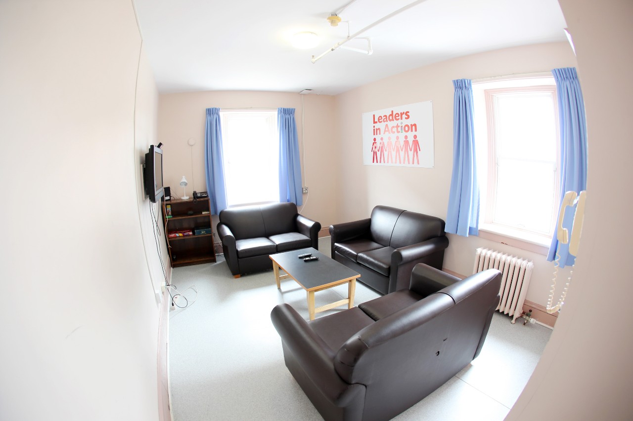 The lounge features comfortable brown sofas and a television on the wall