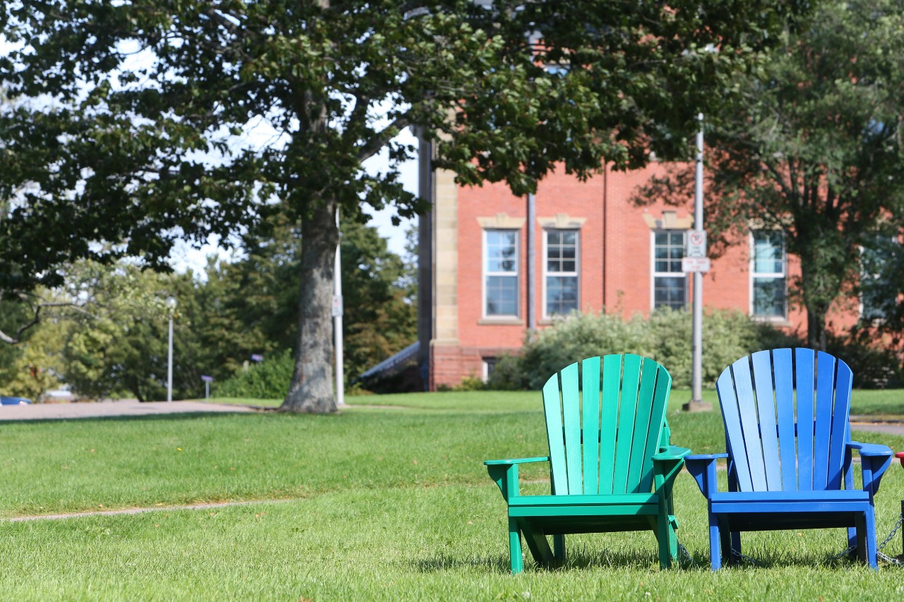 Two Adirondack-style chairs – one green and one blue – sit on the lawn at Dalhousie’s Agricultural Campus in Truro, adjacent to the residences. 