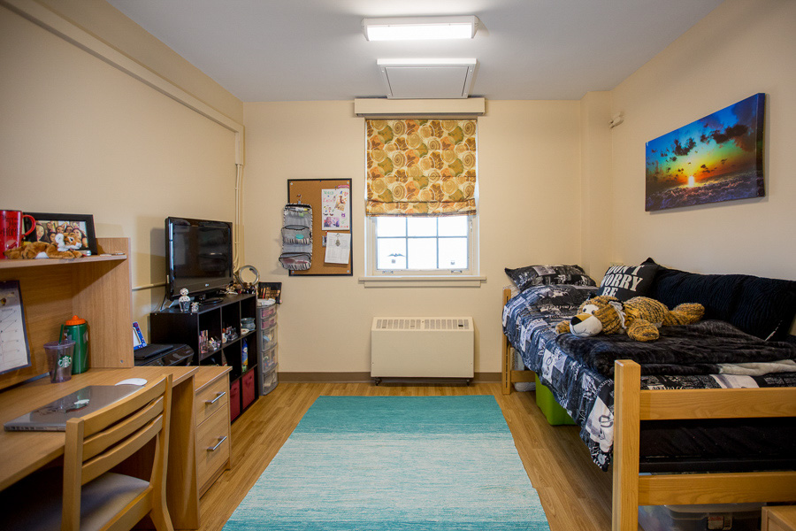 A signal room in Chapman House with a twin bed, desk, chair and storage