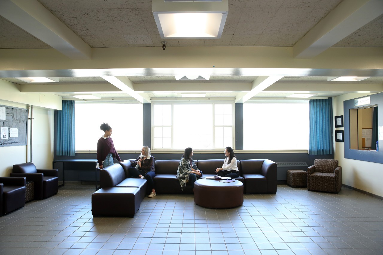 A wide photo of the lobby in Fraser House - including a large brown leather sectional with students seated on it.