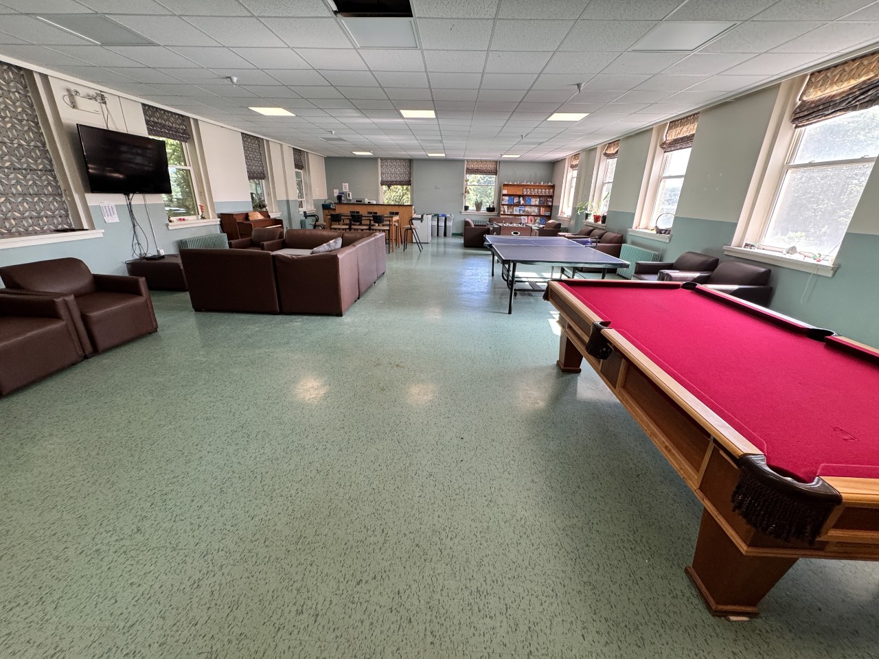 A wide photo of the Trueman House lounge from the front entrance with games tables, a kitchenette, and plenty of seating