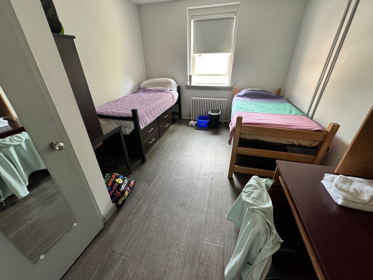 A wide photo of a double room in Trueman House, with a closet, 2 desks, 2 beds, and storage drawers.