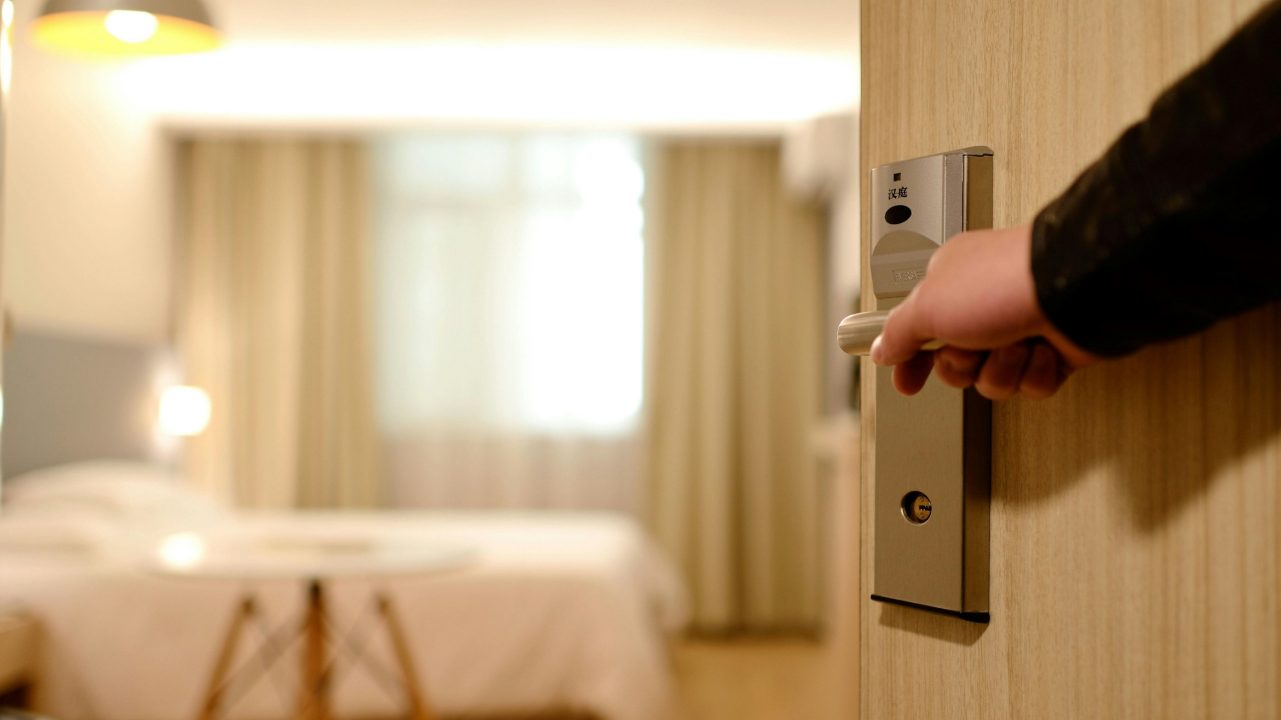 A hand opens the door to a hotel room
