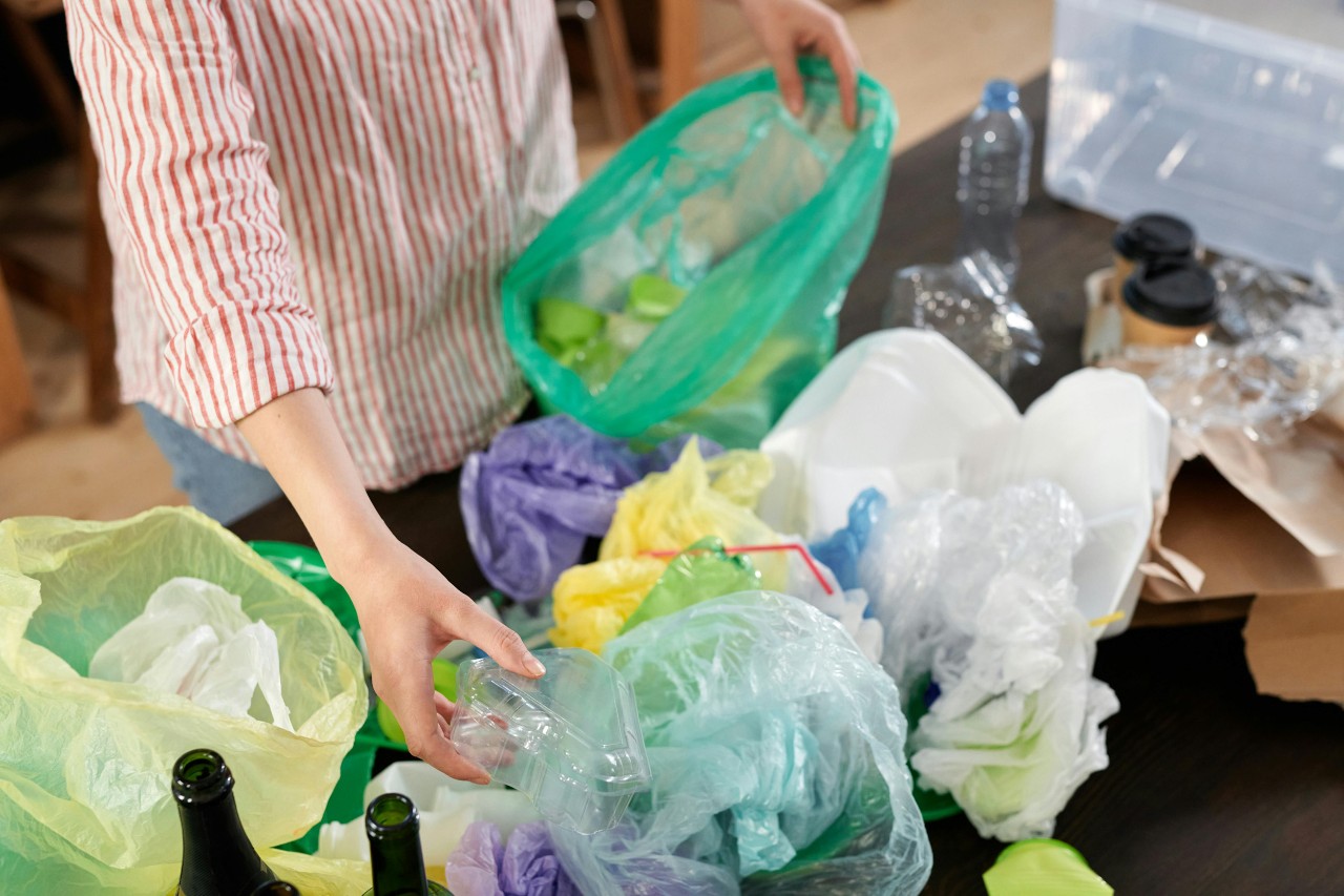 A woman sorts recycling, on a counter, gathering plastic bags