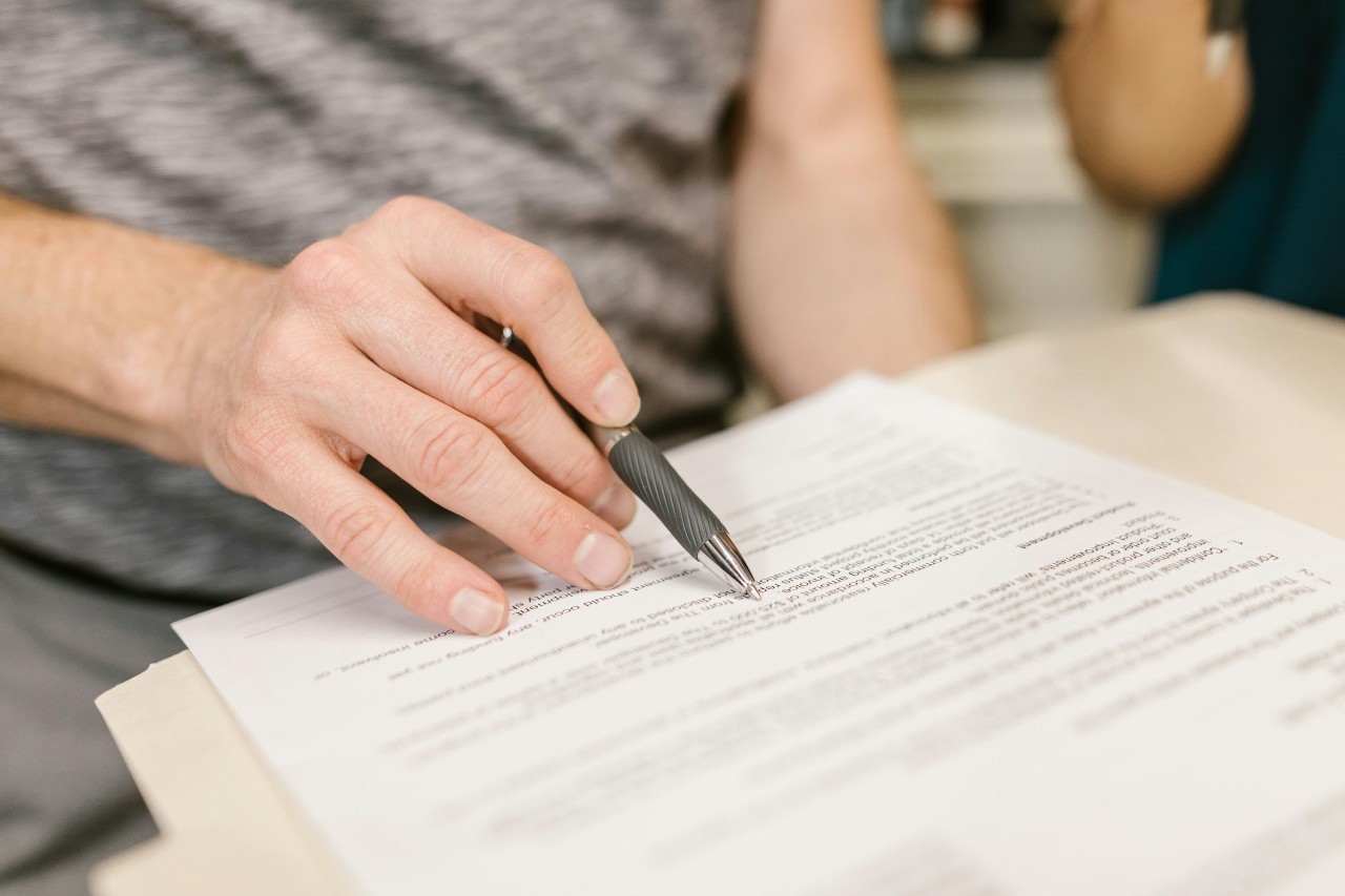 A person reviews a printout of a lease, using a pen to point at words on the paper