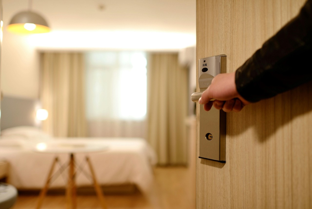 A hand opens the door to a hotel room
