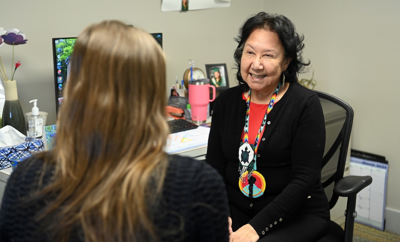 An advisor wearing Indigenous jewellery around her neck smiles at a student who has her back towards the camera.