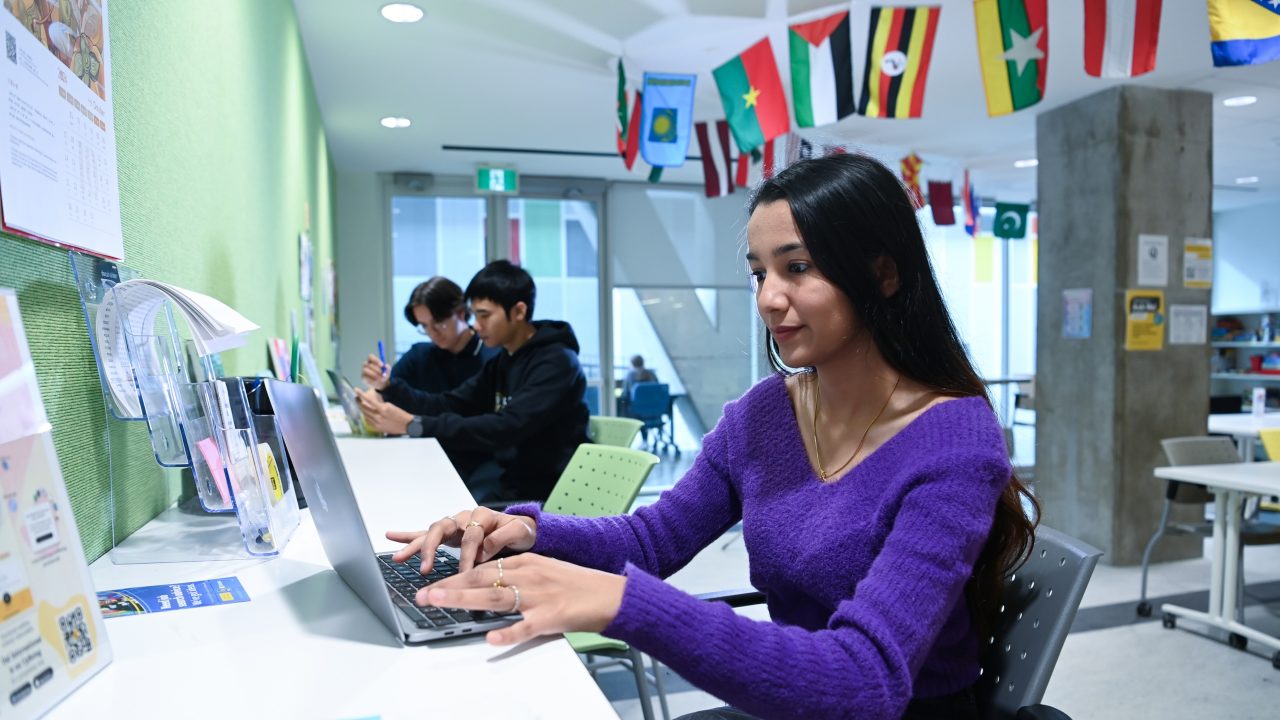 A student wearing a purple shirt working on a laptop at the International Centre at Dalhousie.