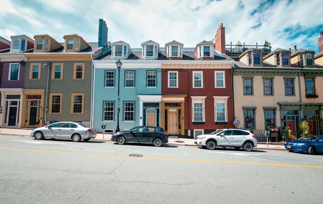 Brightly coloured row houses line a street on a slight incline with cars parked in front of them.