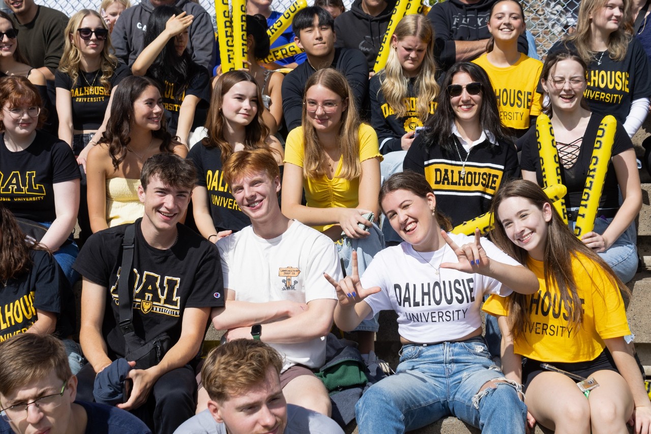 A large group of students wearing black and gold t-shirts that say Dalhousie or Dal smile at the camera.