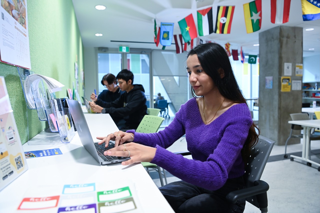 A student wearing a purple shirt working on a laptop at the International Centre at Dalhousie.