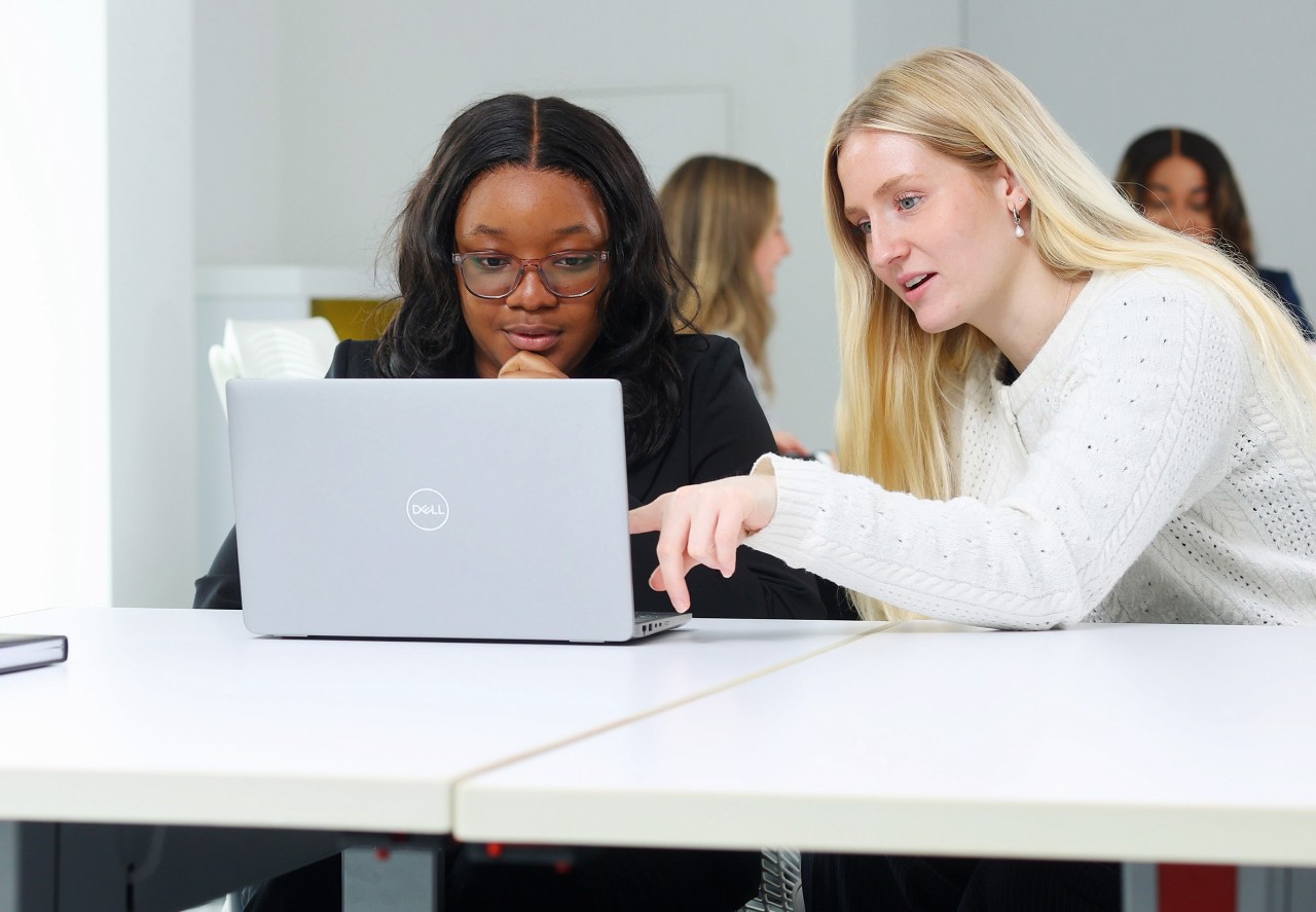 Two students sit at a laptop, discussing what is on the screen. 
