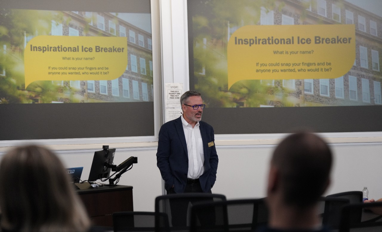 An MBA professor at the front of the class. Screen describes an icebreaker question.