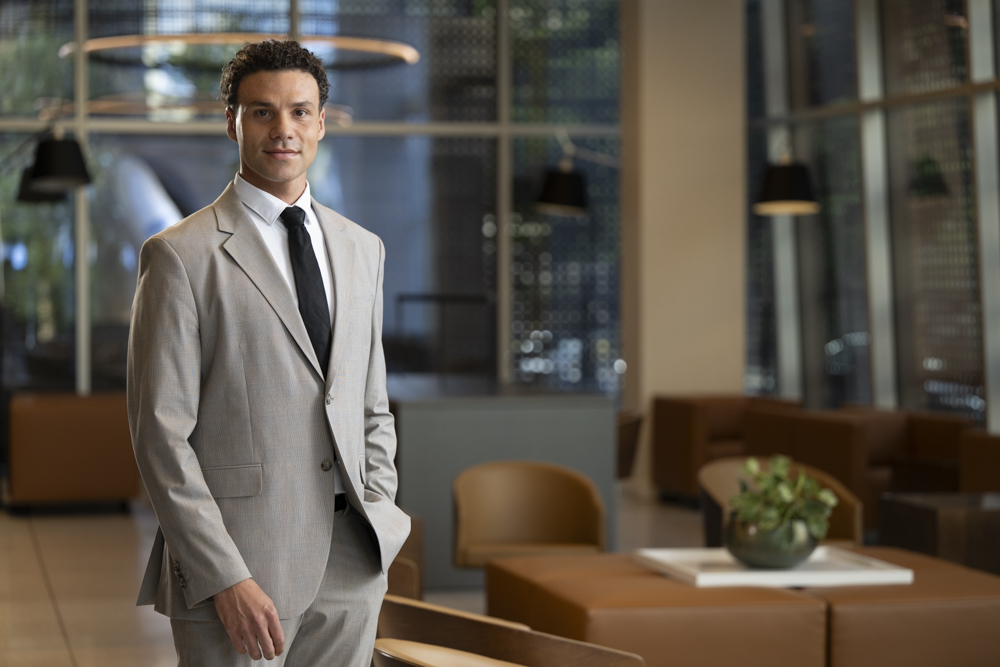 Daniel poses in a light-grey suit in an office.