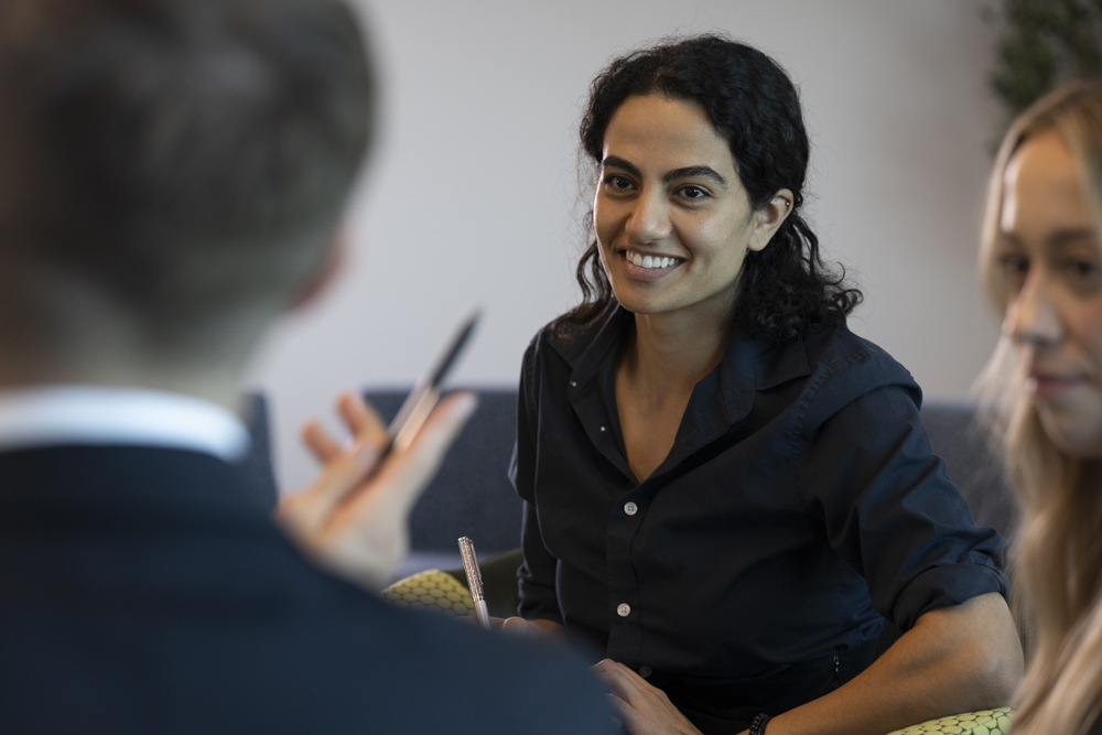 A student leans forward, listening to the student who is facing away from the camera in the foreground. 