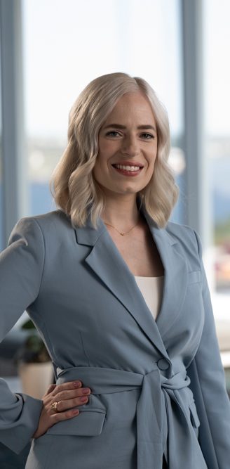 Kristie poses in a blue suit, with a picture window overlooking a harbour behind her.  