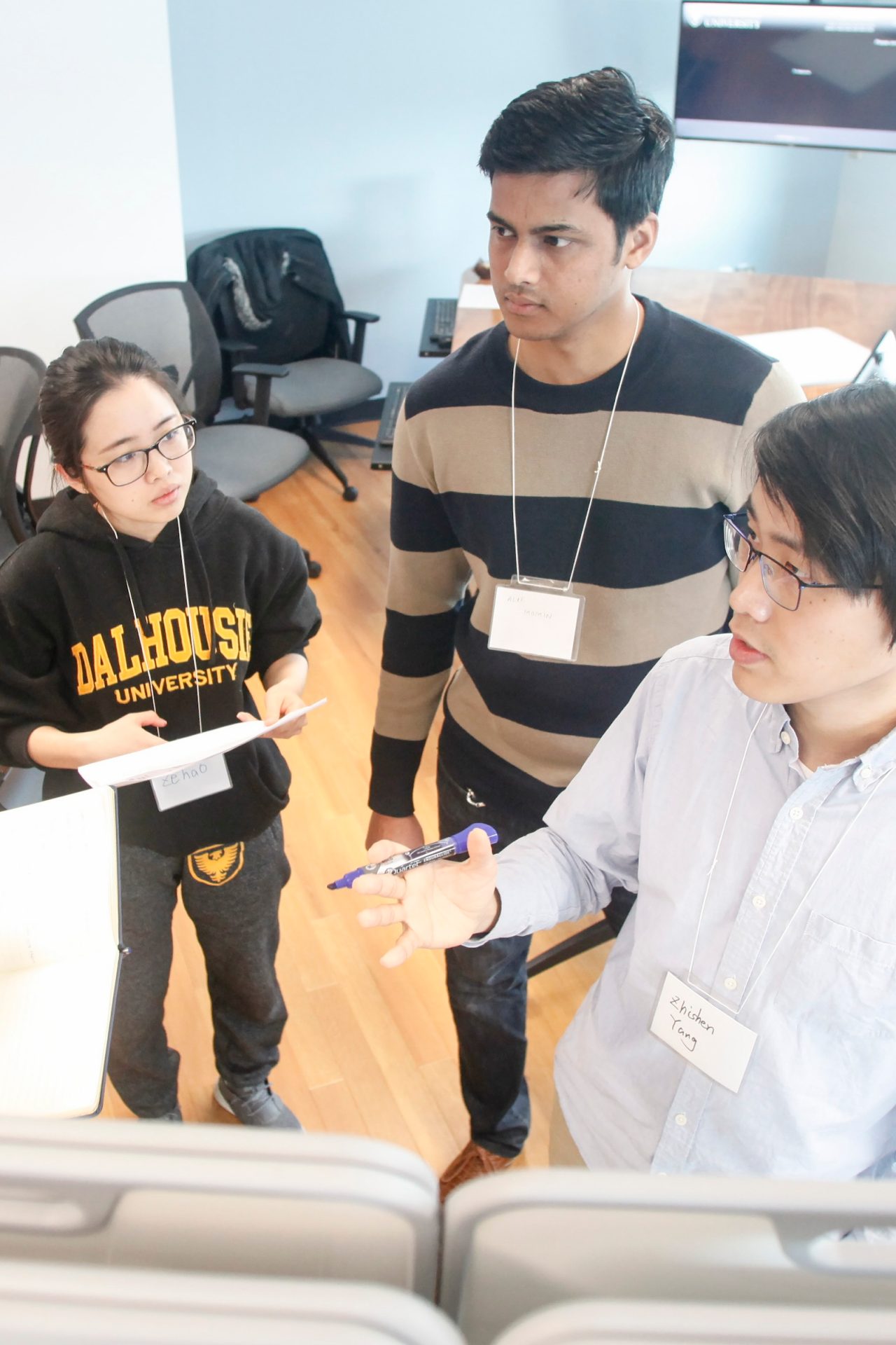 High angle shot of a group of students in an engaged discussion in a room with several screens on the walls and tables. 