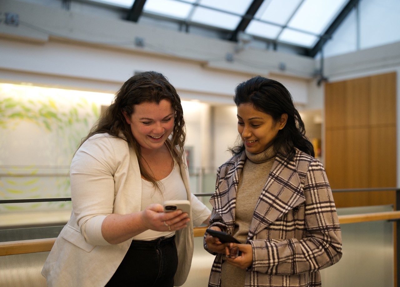 Two students smile at each other as they compare information on their phones.