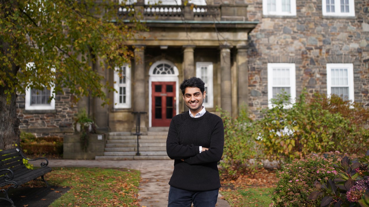 An MPA student stands in front of a brick building, smiling with his arms crossed.  