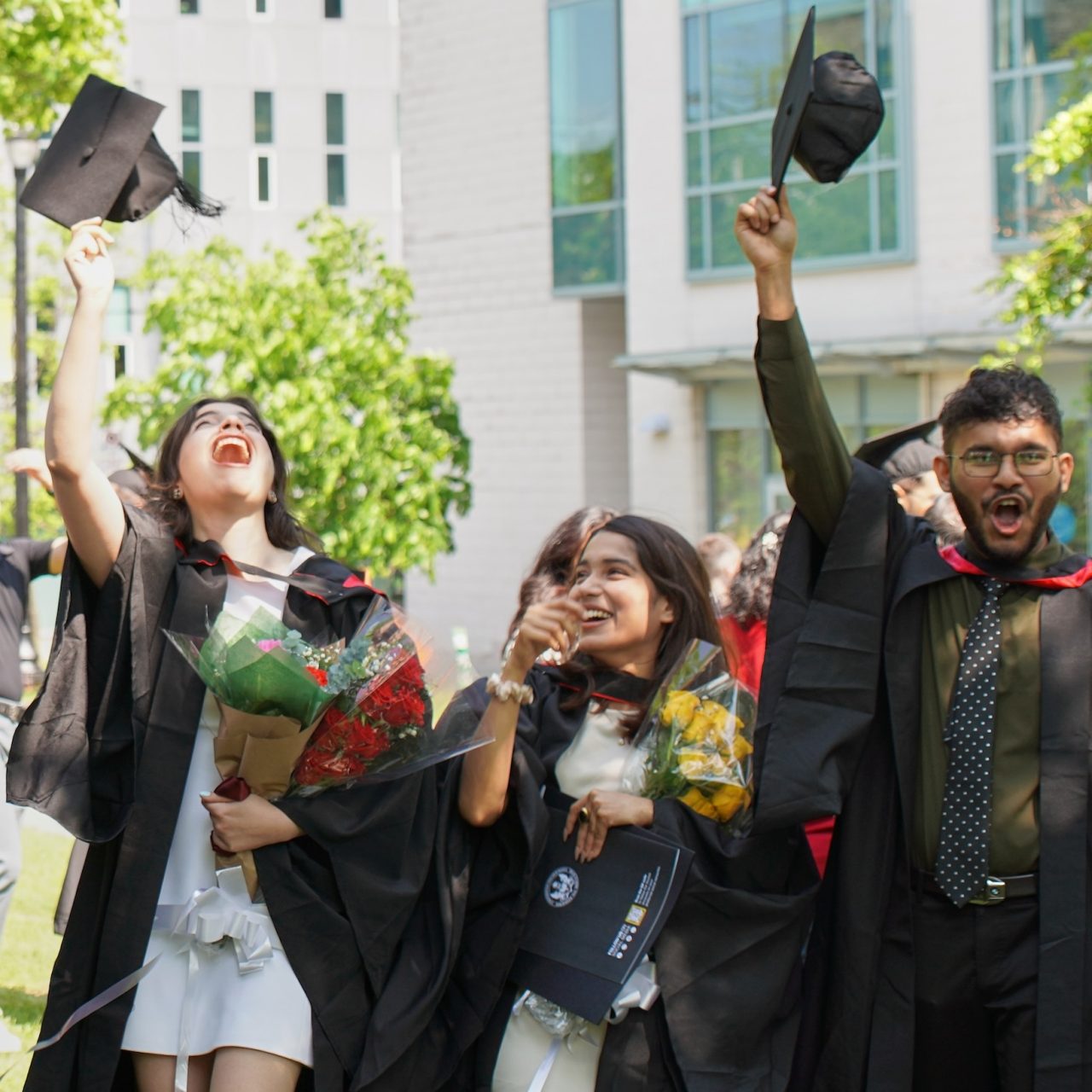 A group of students wearing convocation gowns cheering and throwing their caps in the air.  