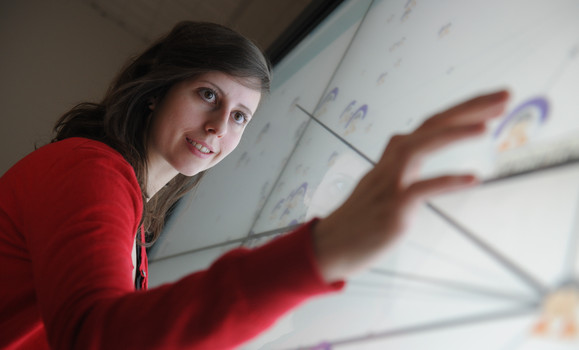 A person in a red sweater faces a large touch screen showing a chart with their fingers on a picture to move it.