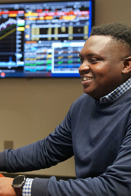 A student sits at a computer with a multi-coloured keyboard. Screens in the background show tables and charts.  