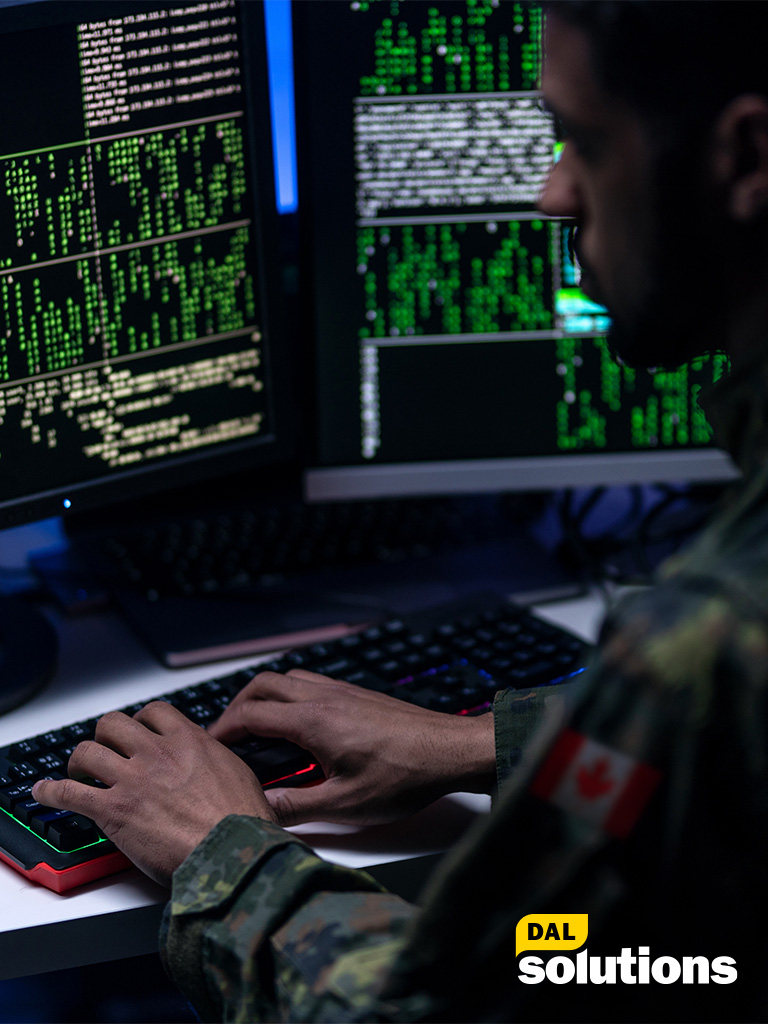 A man is typing on the keyboard facing two computer screens
