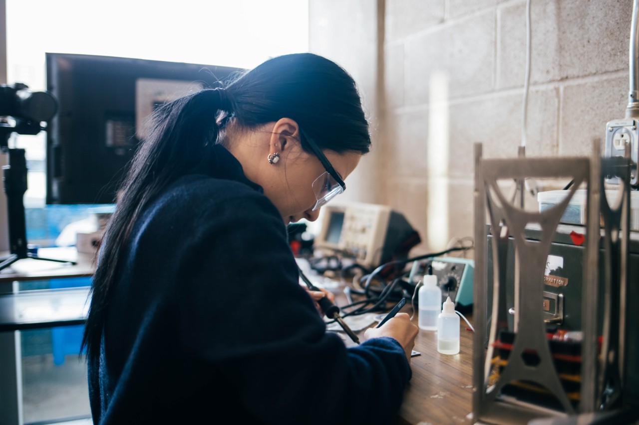 Dal student wearing safety glasses, using a soldering tool at a workstation