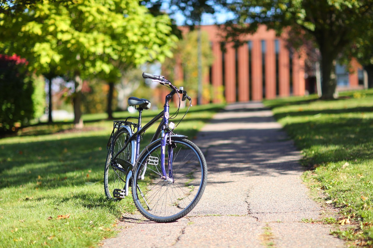 Blue bicycle on the path in front of a red brick building with a row of long vertical windows.