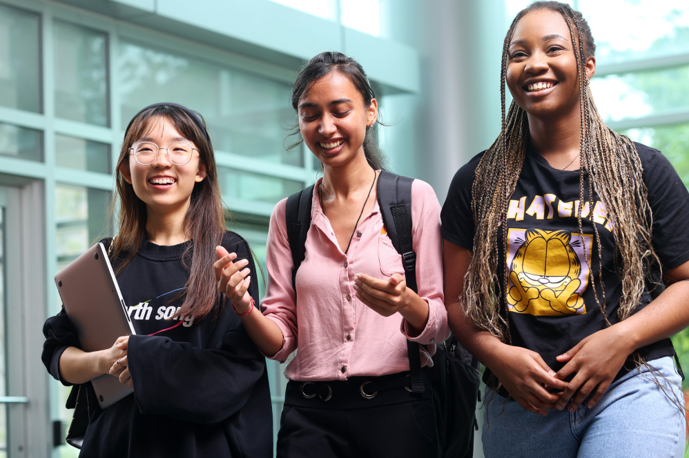 Three students chat as they walk through the lobby of the Rowe Management Building.