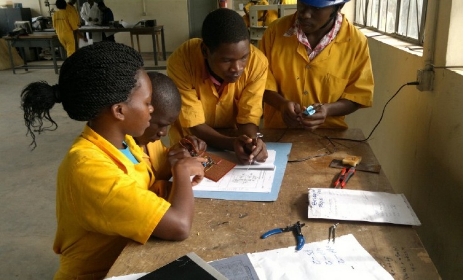 A Ugandan girl and three men wearing bright yellow shirts stand around a table. On the table, there are tools and notebooks. 