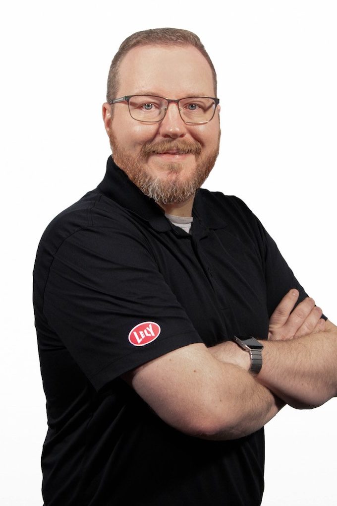 Smiling man wearing glasses and a black polo shirt poses with his arms crossed.