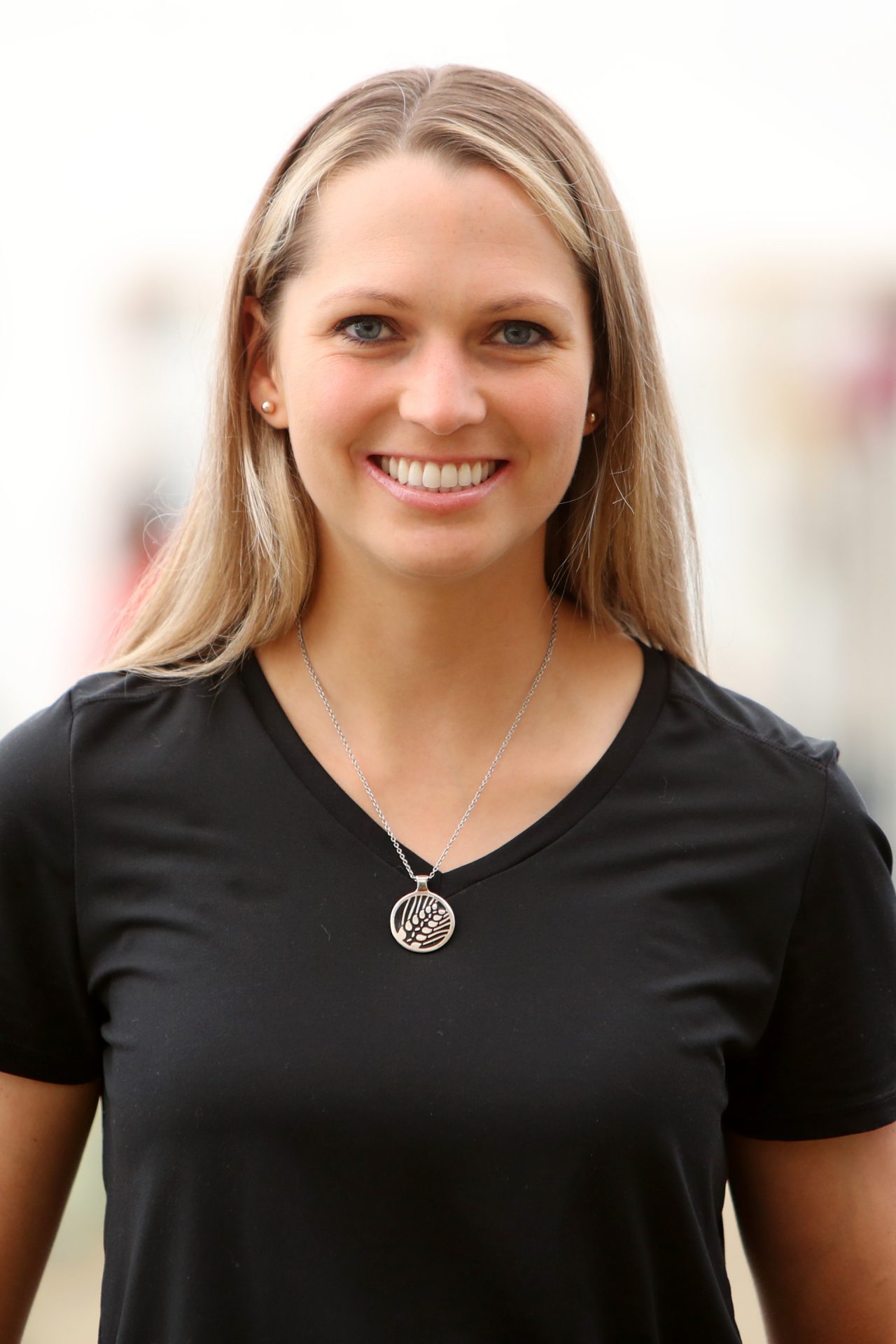 Smiling woman with long blond hair wearing a silver pendant and black t-shirt.