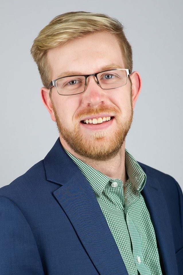 Man with blond hair and metal glasses wearing a blue blazer and a green checked shirt.