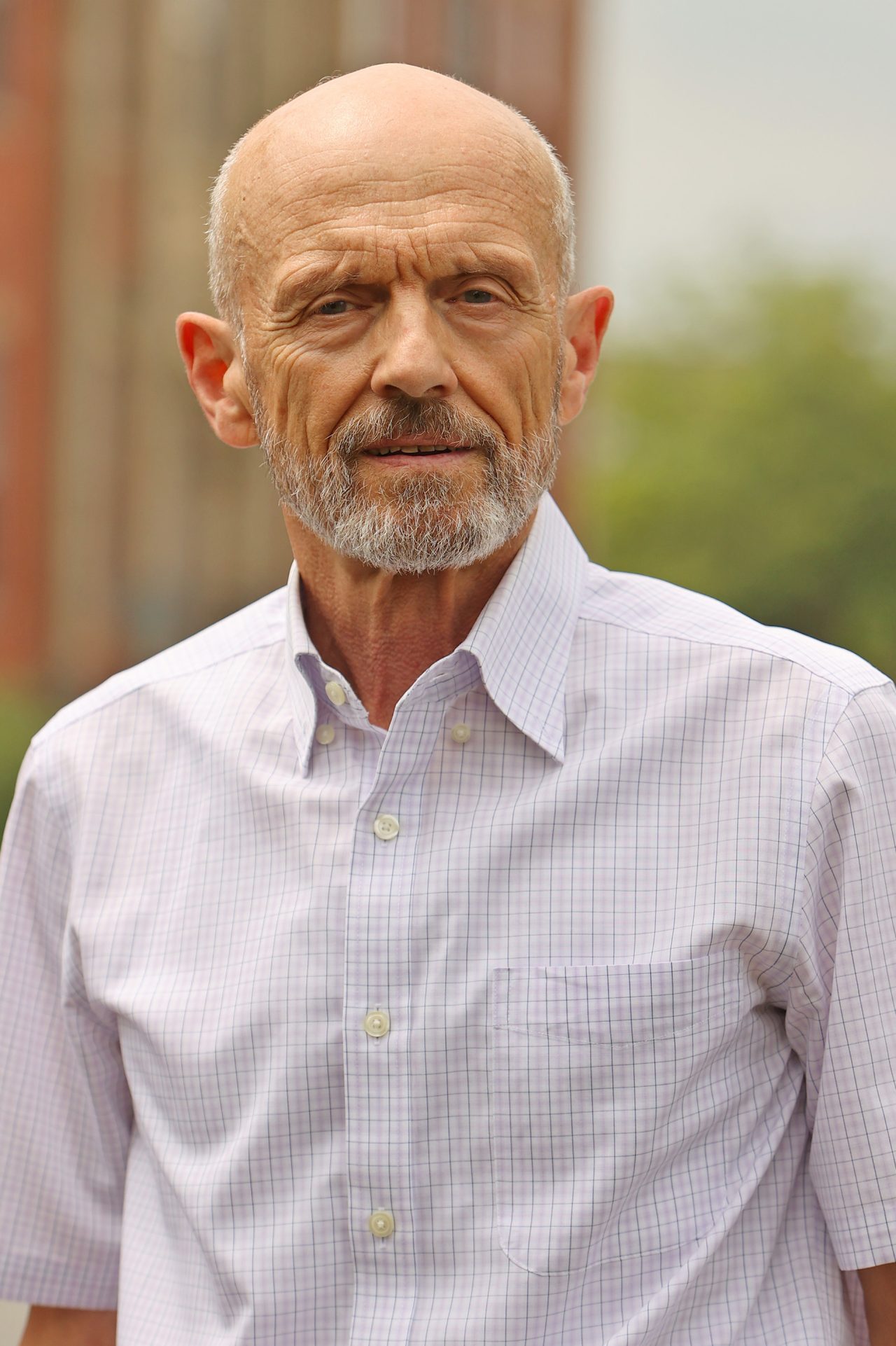 Man with short grey hair and beard wearing a checked shirt.