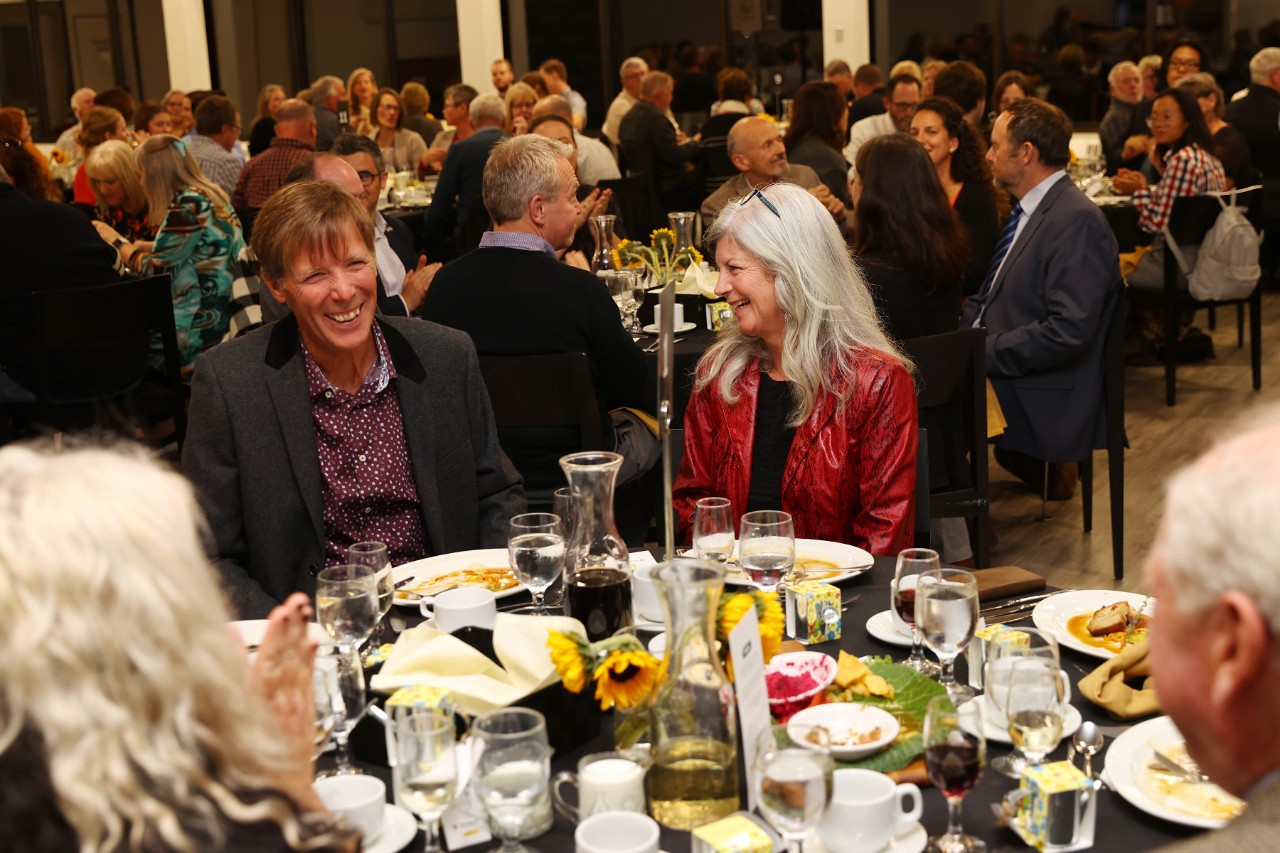 Groups of people dining at round tables in a large event hall.