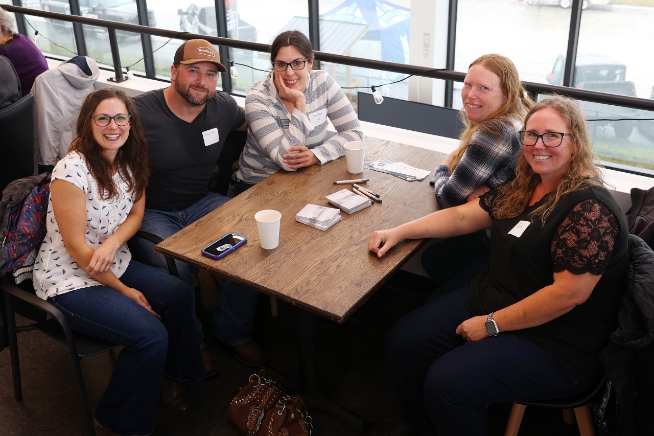 A group of casually dressed alumni sitting around a table smiling.