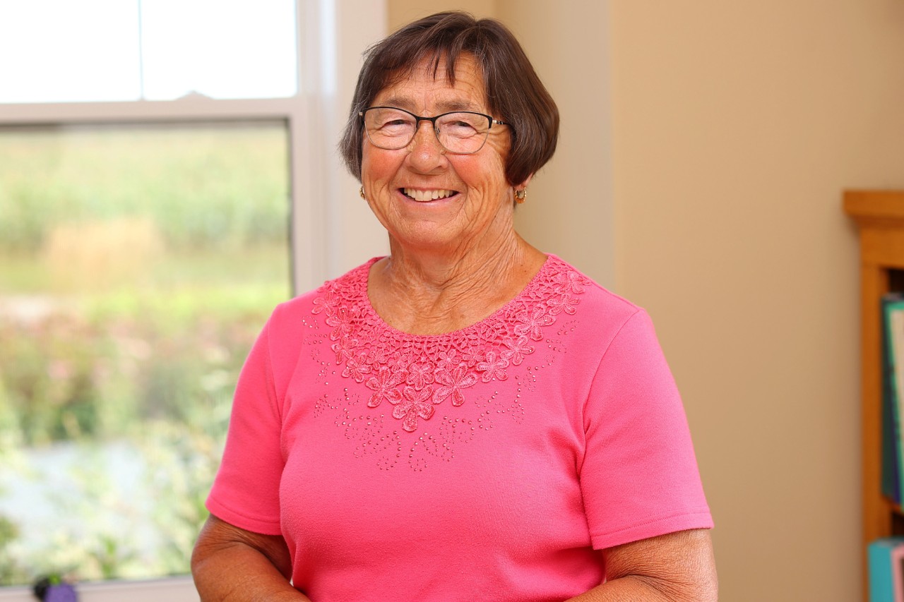 Headshot of carol Versteeg, she is smiling, wearing glasses and a pink shirt
