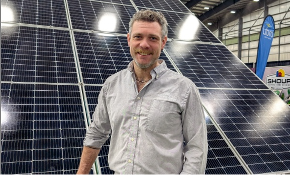 Man wearing a grey shirt stands in front of solar panels.