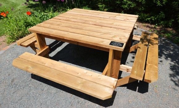 Brown wood picnic table seats on four sides in a garden setting.