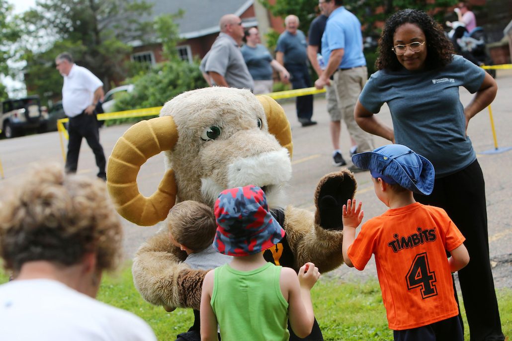 Ram mascot kneels to give two children high-fives.