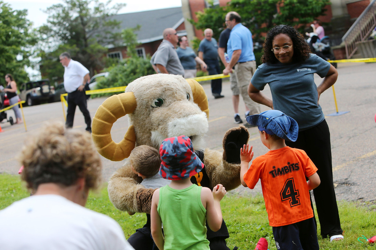 Ram mascot kneels to give two children high-fives.