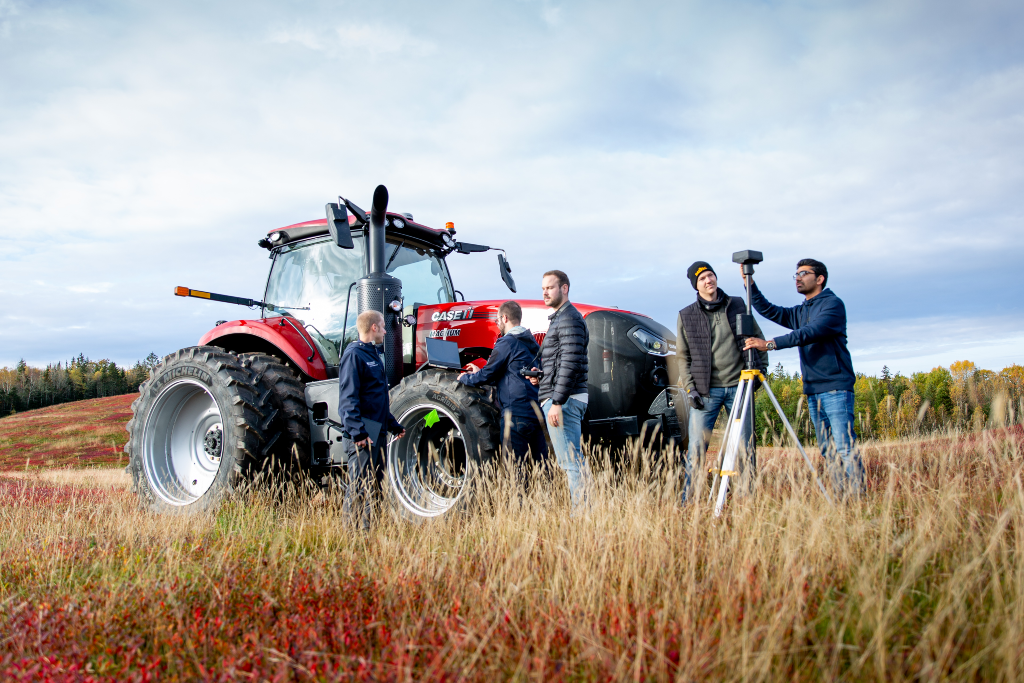 A group of students setting up equipment around a red tractor in a field