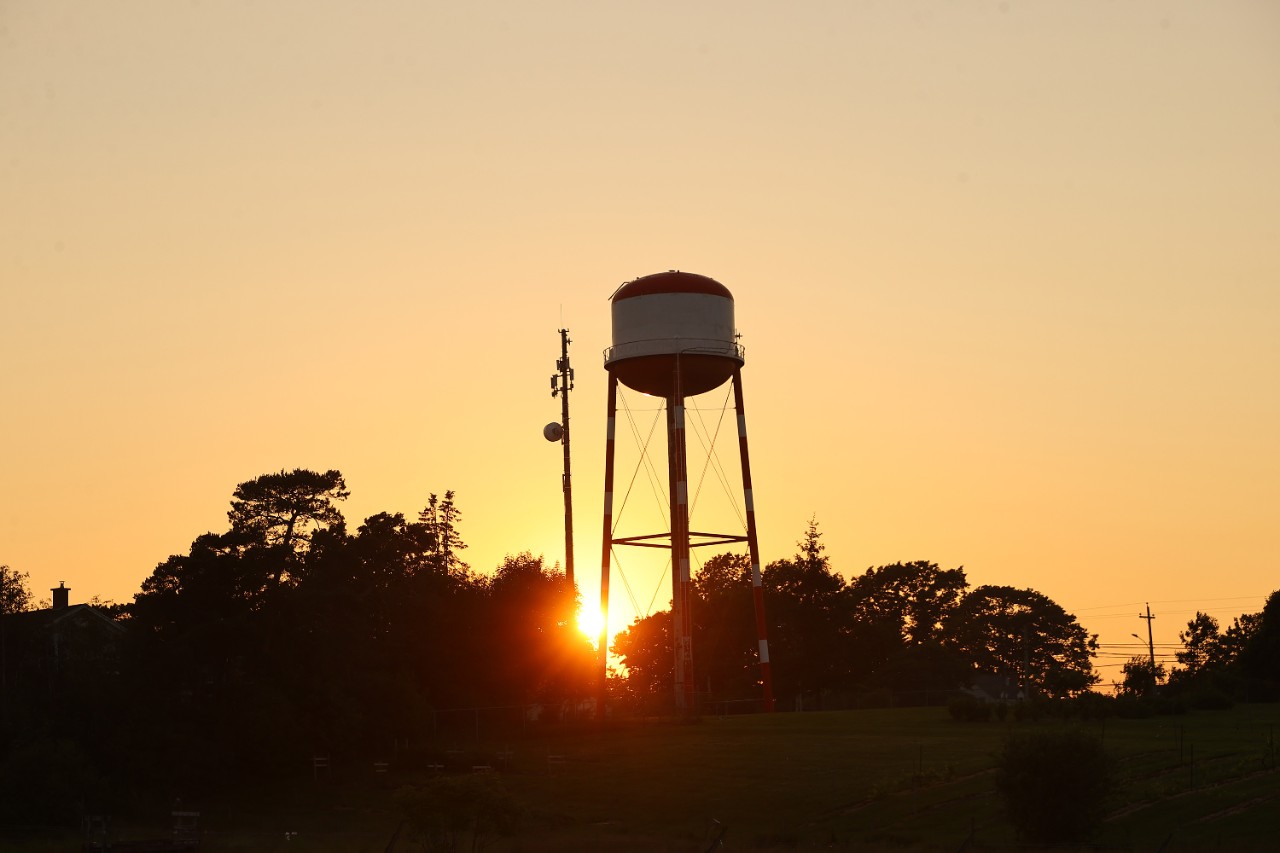 Silhouette of a water tower against an orange sunrise.