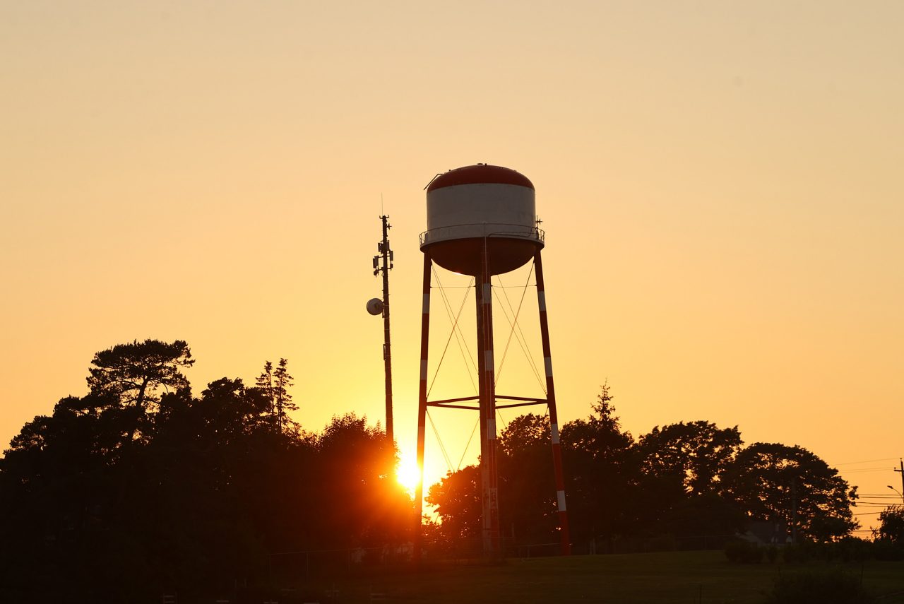 Silhouette of a water tower against an orange sunrise.