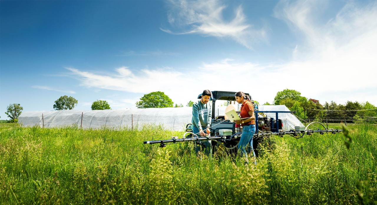Two students in a green field working on a tractor. 