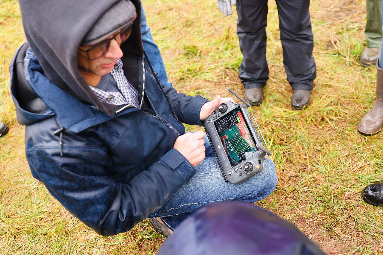An instructor in a field holding the controls to a sprayer drone