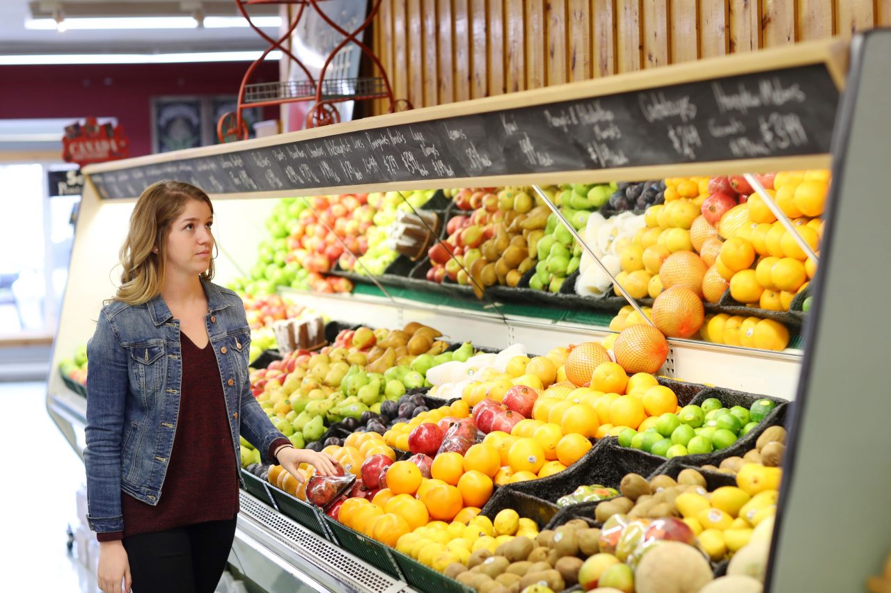 A woman looks at prices of fruit in a grocery isle. 