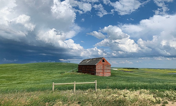 Red barn in a green field under a cloudy sky.
